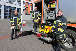 Foto: Auszubildende der Feuerwehr vor einem Feuerwehrfahrzeug mit Geräten in der Hand