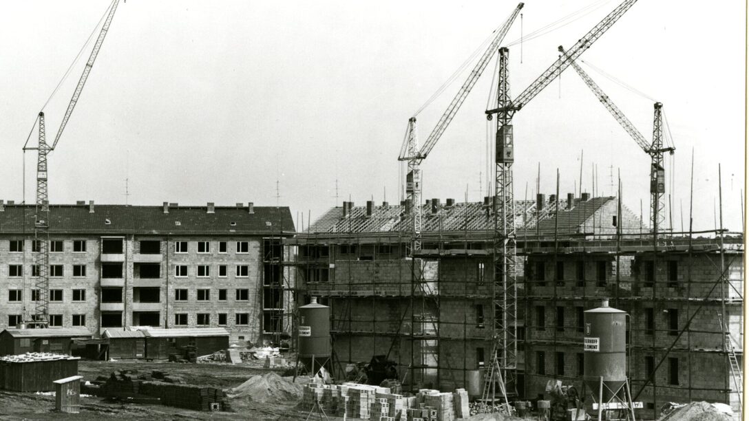 Ein Schwarz-Weiß-Bild welches den Bau des Berliner Viertels in Rüsselsheim zeigt. Zwei im Bau befindliche mehrgeschossige Häuser mit Baugerüst und mehreren Baukränen.