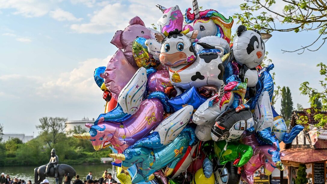 Zusammengebundende Heliumluftballons. Im Hintergund Buden, Passanten und der Leinreiter am Main.