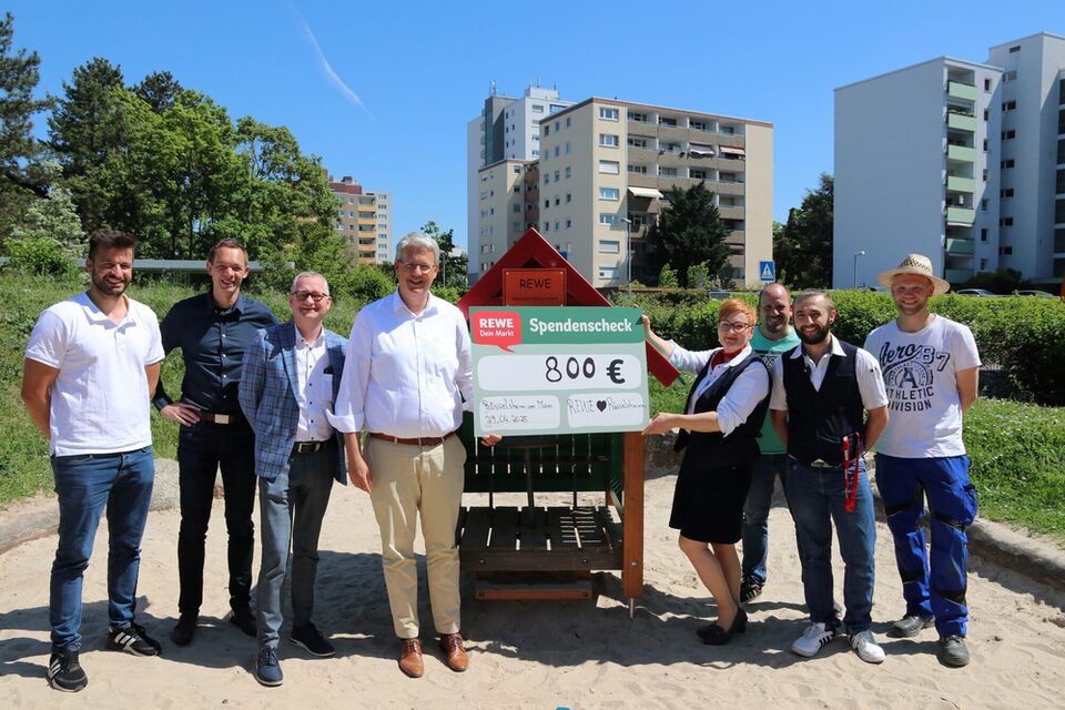 Das Rewe-Team übergibt vor dem neuen Spielhaus einen Spendencheck.