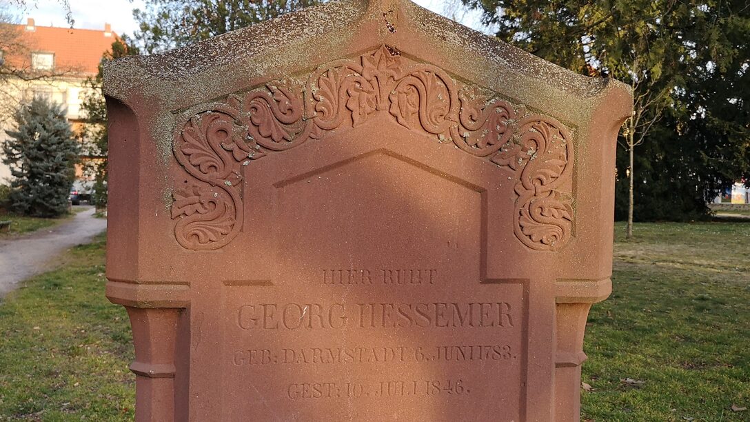 Grabstein mit der Aufschrift "Hier ruht Georg Hessemer". Im Hintergrund grüner Rasen und Bäume.