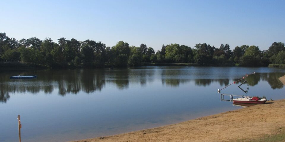 Der See des Waldschwimmbads mit Ufer, Bäumen und Rettungs-Tretboot