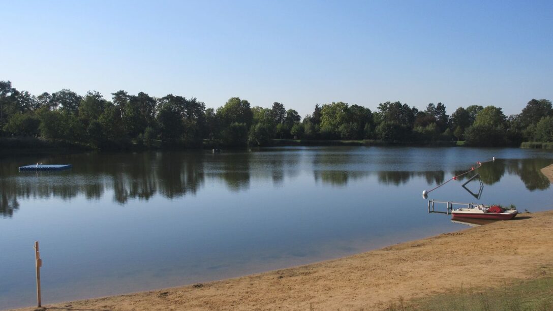 Der See des Waldschwimmbads mit Ufer, Bäumen und Rettungs-Tretboot