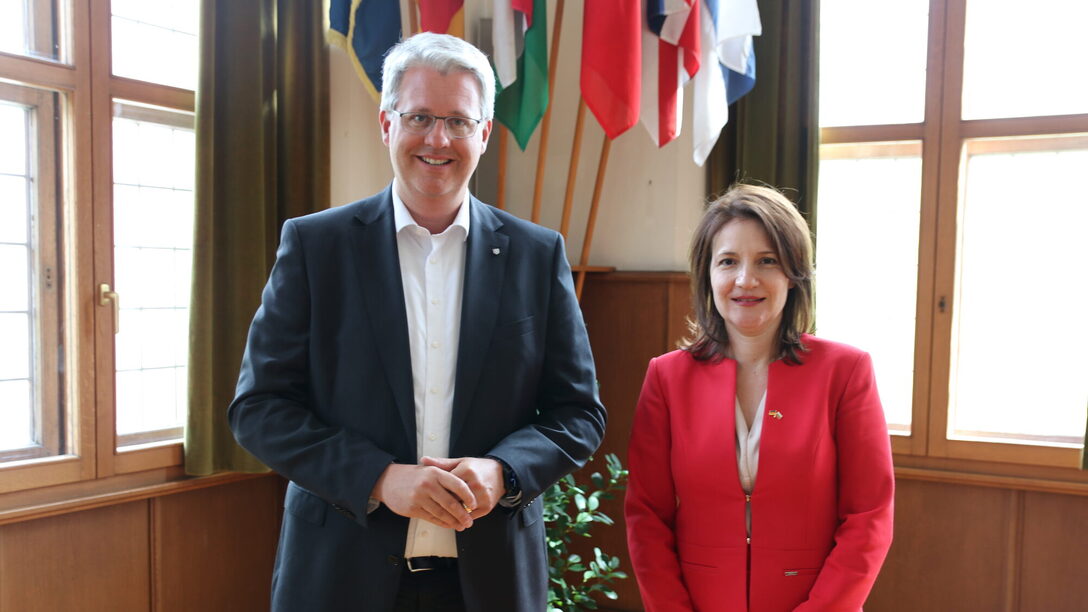 Oberbürgermeister Patrick Burghardt und Generalkonsulin Diana Popova stehen vor den internationalen Fahnen im historischen Sitzungssaal.