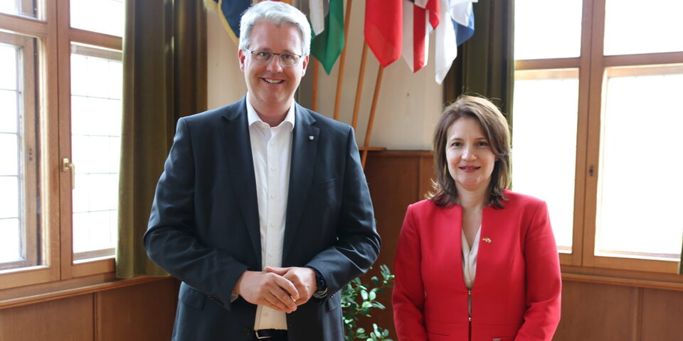 Oberbürgermeister Patrick Burghardt und Generalkonsulin Diana Popova stehen vor den internationalen Fahnen im historischen Sitzungssaal.