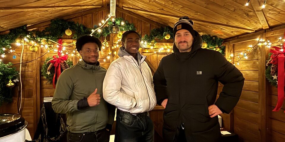 In einer Verkaufshütte auf dem Weihnachtsmarkt in Évreux (v.l.n.r.): Die beiden Praktikanten Yves und Yael sowie Lucas Fischer vom Veranstaltungswesen der Stadt Rüsselsheim am Main.