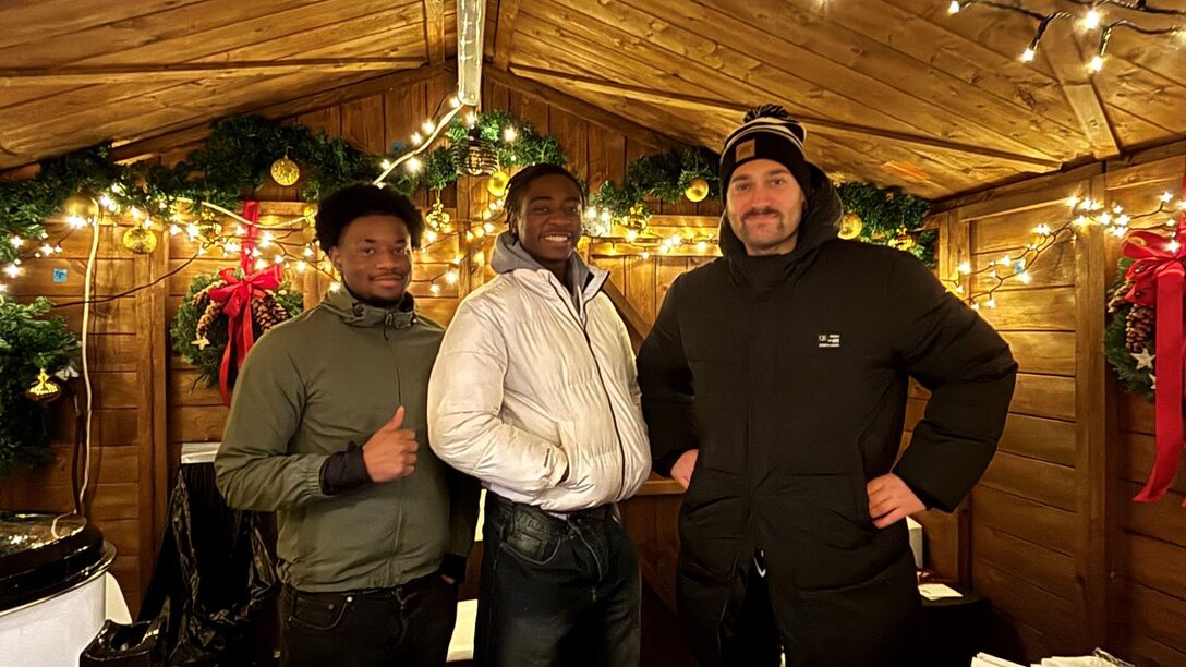 In einer Verkaufshütte auf dem Weihnachtsmarkt in Évreux (v.l.n.r.): Die beiden Praktikanten Yves und Yael sowie Lucas Fischer vom Veranstaltungswesen der Stadt Rüsselsheim am Main.