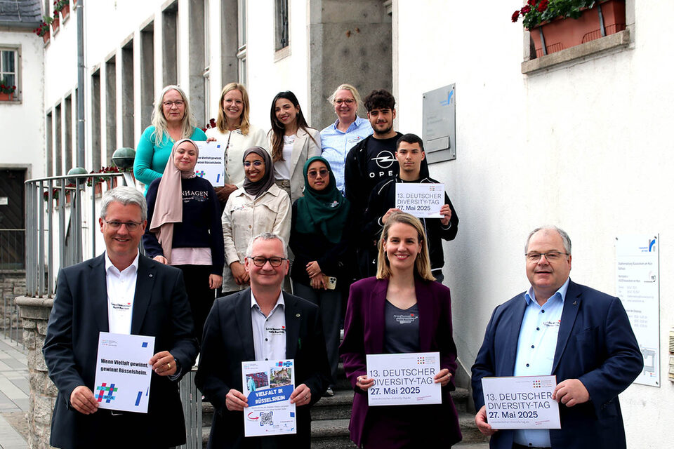 Mitglieder des Unterzeichner-Netzwerk der Charta der Vielfalt in Rüsselsheim halten Schilder zum "Diversity Tag 2025" hoch vor dem Rathaus.