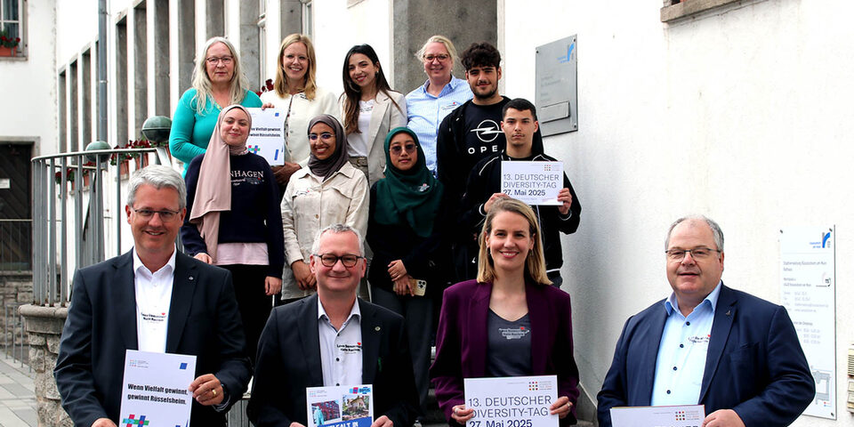 Mitglieder des Unterzeichner-Netzwerk der Charta der Vielfalt in Rüsselsheim halten Schilder zum "Diversity Tag 2025" hoch vor dem Rathaus.
