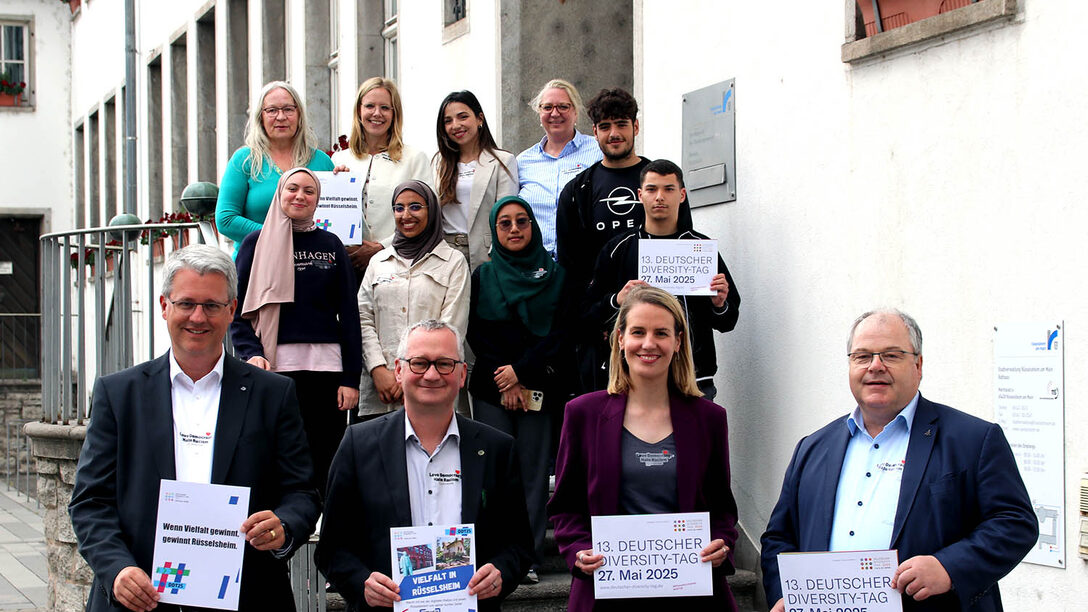 Mitglieder des Unterzeichner-Netzwerk der Charta der Vielfalt in Rüsselsheim halten Schilder zum "Diversity Tag 2025" hoch vor dem Rathaus.