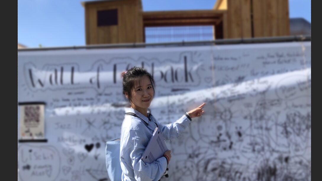 Eine Person steht vor einer weißen Wand, in Schwarz stehen auf der Wand Zeichnungen und Texte. Oben links steht "Wall of Feedback"