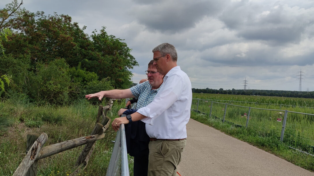Harald Lehmann vom Amt für Umwelt und Klimaschutz und Oberbürgermeister Patrick Burghardt stehen an der Sanddüne in Bauschheim. Im Hintergrund ein Feldweg und die abgezäunte Erweiterungsfläche.