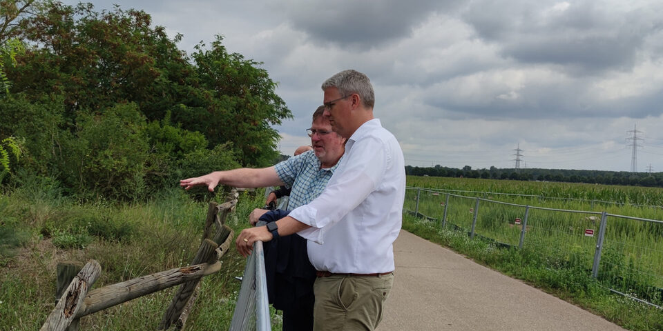 Harald Lehmann vom Amt für Umwelt und Klimaschutz und Oberbürgermeister Patrick Burghardt stehen an der Sanddüne in Bauschheim. Im Hintergrund ein Feldweg und die abgezäunte Erweiterungsfläche.