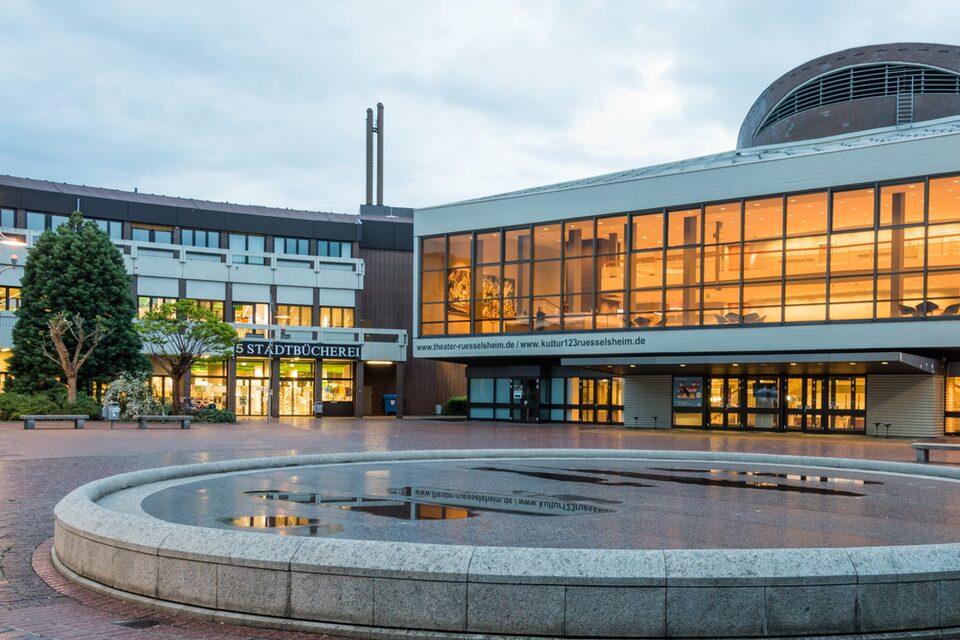 Blick auf das erleuchtete Theater und die Stadtbücherei. Im Vordergrund der stillgelegte Brunnen.