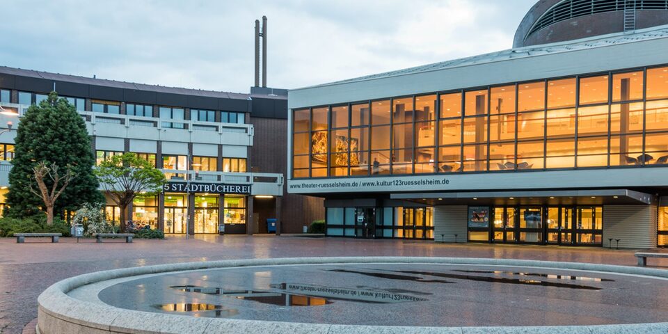 Blick auf das erleuchtete Theater und die Stadtbücherei. Im Vordergrund der stillgelegte Brunnen.