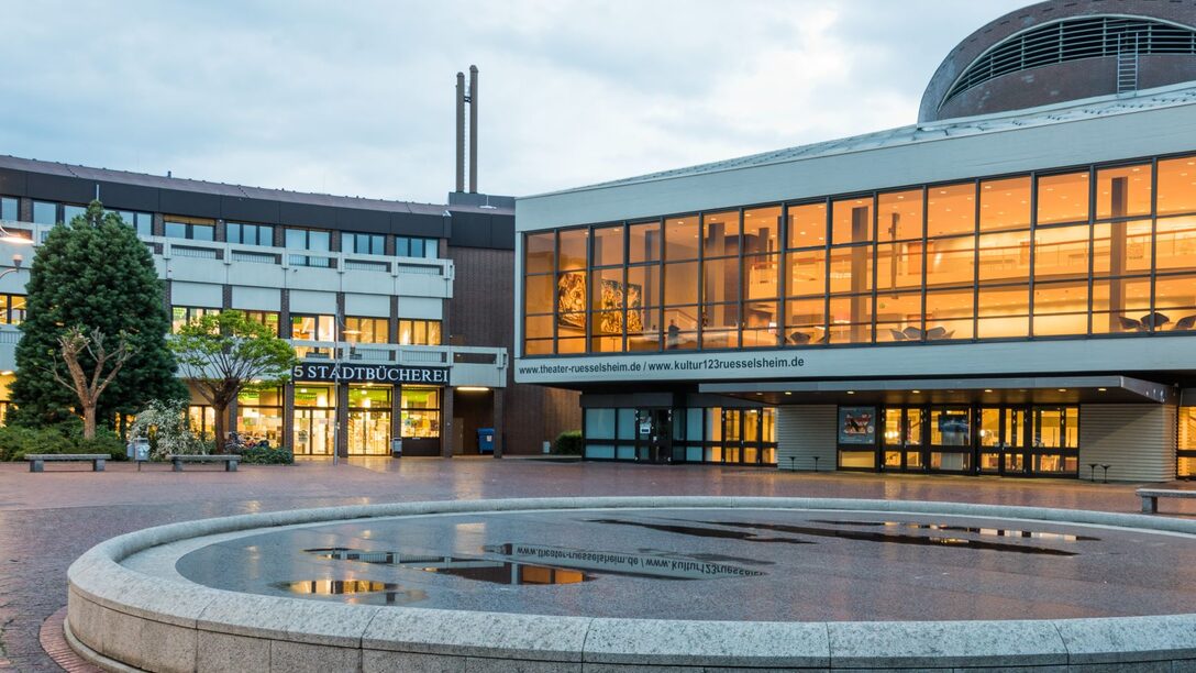 Blick auf das erleuchtete Theater und die Stadtbücherei. Im Vordergrund der stillgelegte Brunnen.