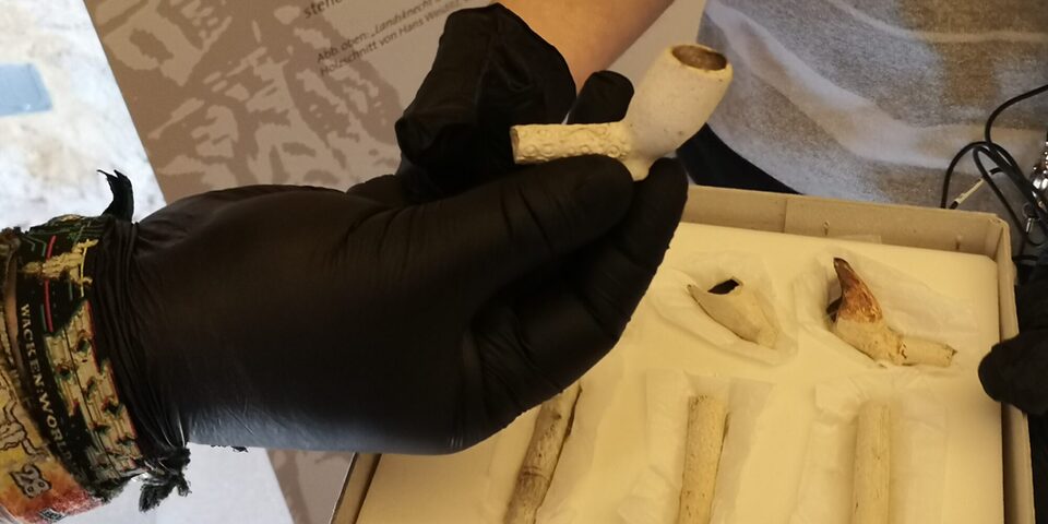 Mit einem Handschuh wird eine Keramikpfeife gezeigt.