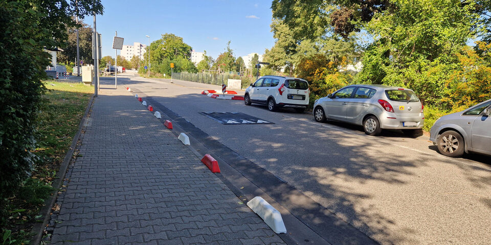 Rote und weiße Schwellen sichern den Gehweg ab, eine Schwelle auf der Fahrbahn reduziert die Geschwindigkeit.
