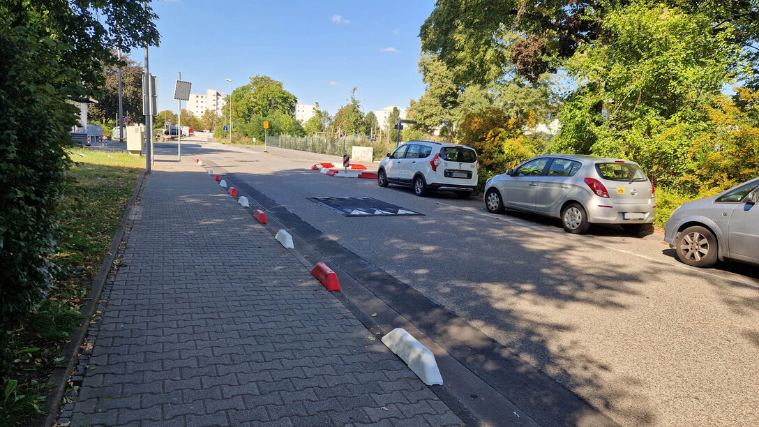 Rote und weiße Schwellen sichern den Gehweg ab, eine Schwelle auf der Fahrbahn reduziert die Geschwindigkeit.
