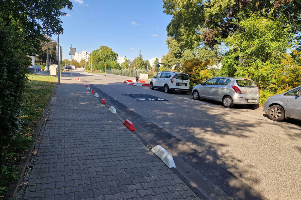 Rote und weiße Schwellen sichern den Gehweg ab, eine Schwelle auf der Fahrbahn reduziert die Geschwindigkeit.
