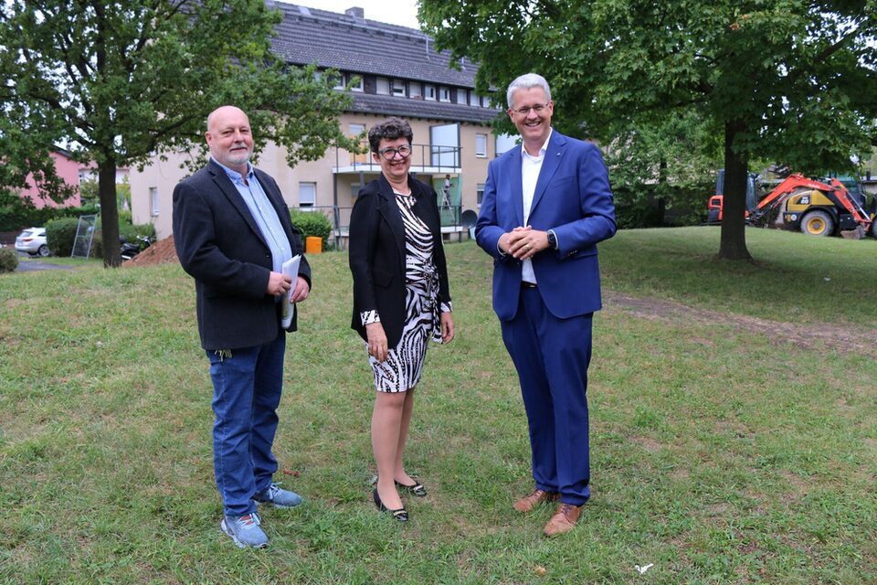 Projektleiter, Vorständin und Oberbürgermeister stehen auf einer Wiese vor einem Modernisierungsobjekt.