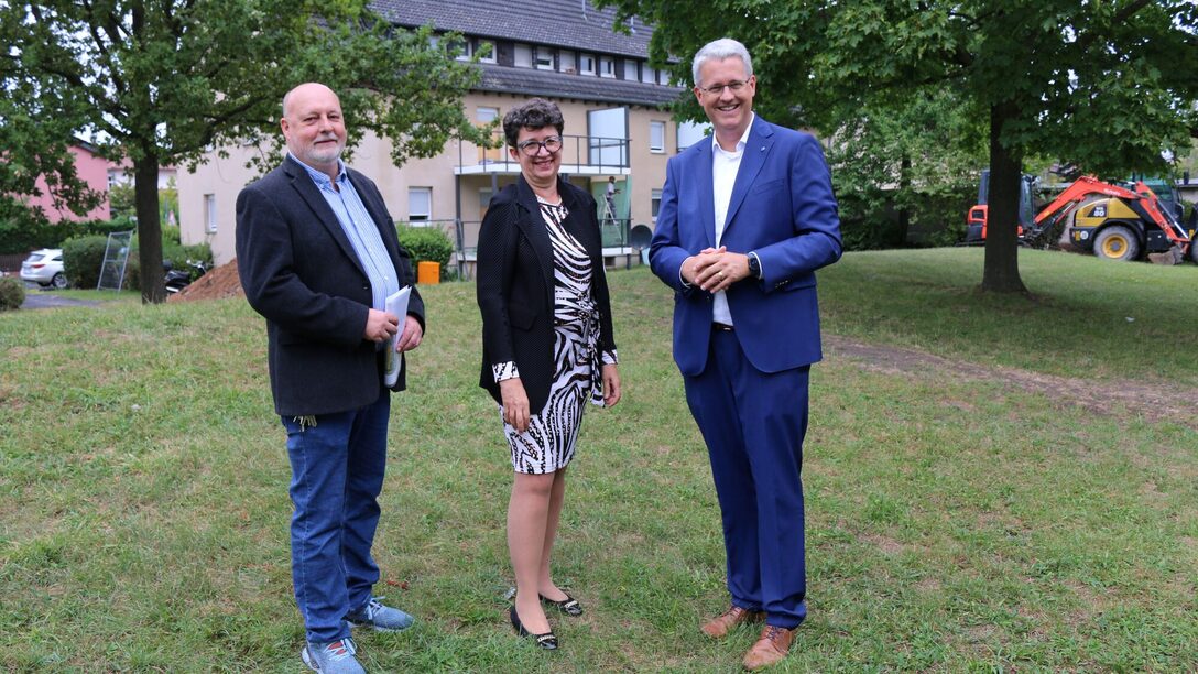 Projektleiter, Vorständin und Oberbürgermeister stehen auf einer Wiese vor einem Modernisierungsobjekt.