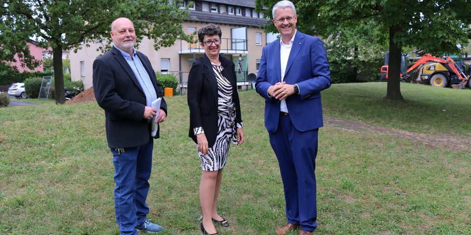 Projektleiter, Vorständin und Oberbürgermeister stehen auf einer Wiese vor einem Modernisierungsobjekt.