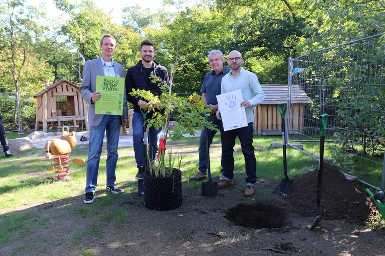 Stadtrat Valerius zeigt ein Zertifikat, wie viel Kohlendioxid, auf beiden Spielplätzen in der Erde gebunden werden konnte.