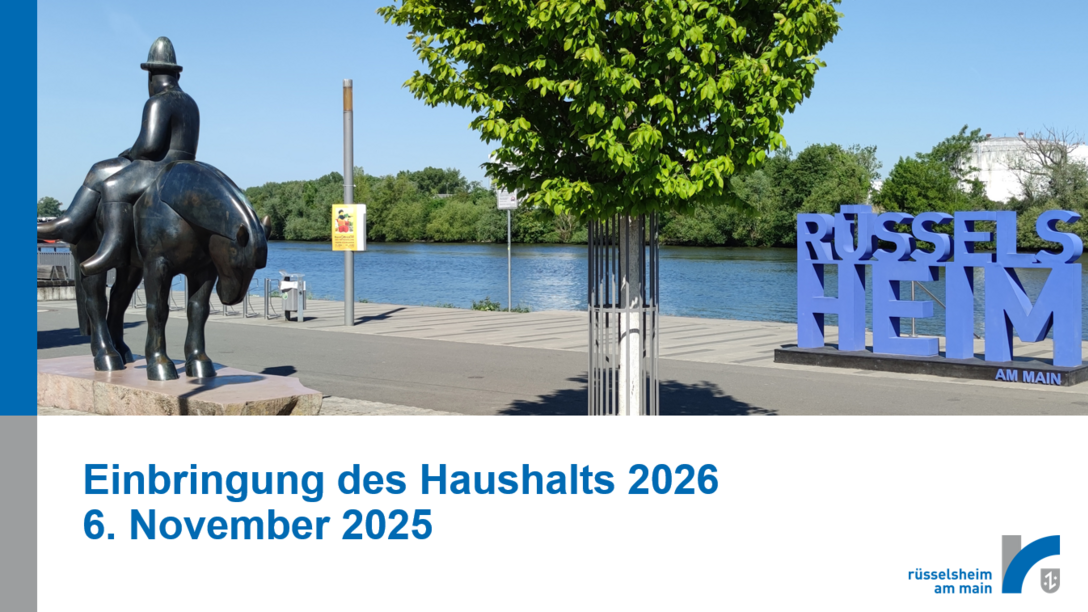 Deckblatt einer Powerpoint-Präsentation mit der Aufschrift "Einbringung des Haushalts 2026, 6. November 2025" und einem Foto, das den Main, den Leinreiter und den Rüsselsheim-Schriftzug im Sommer zeigt.