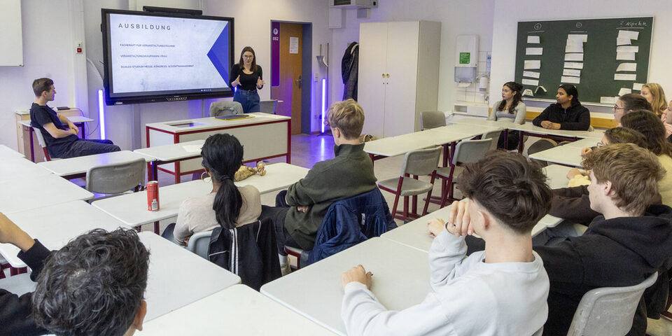 Unternehmen stellen sich vor: Schüler sitzen in einem Klassenraum. An einem Whiteboard läuft eine Präsentation.