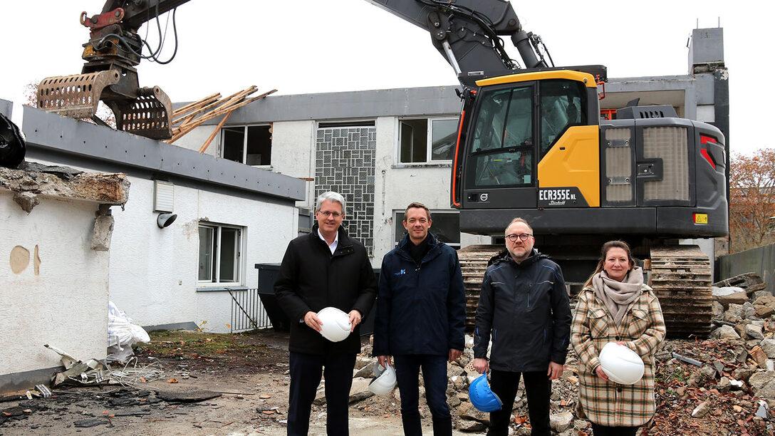 Im Hintergrund ein Bagger und halb abgerissenes Gebäude. Davor stehen: Oberbürgermeister Patrick Burghardt, Stadtrat Simon Valerius, Daniel Langer und Anna Steeg von der Stadtverwaltung.