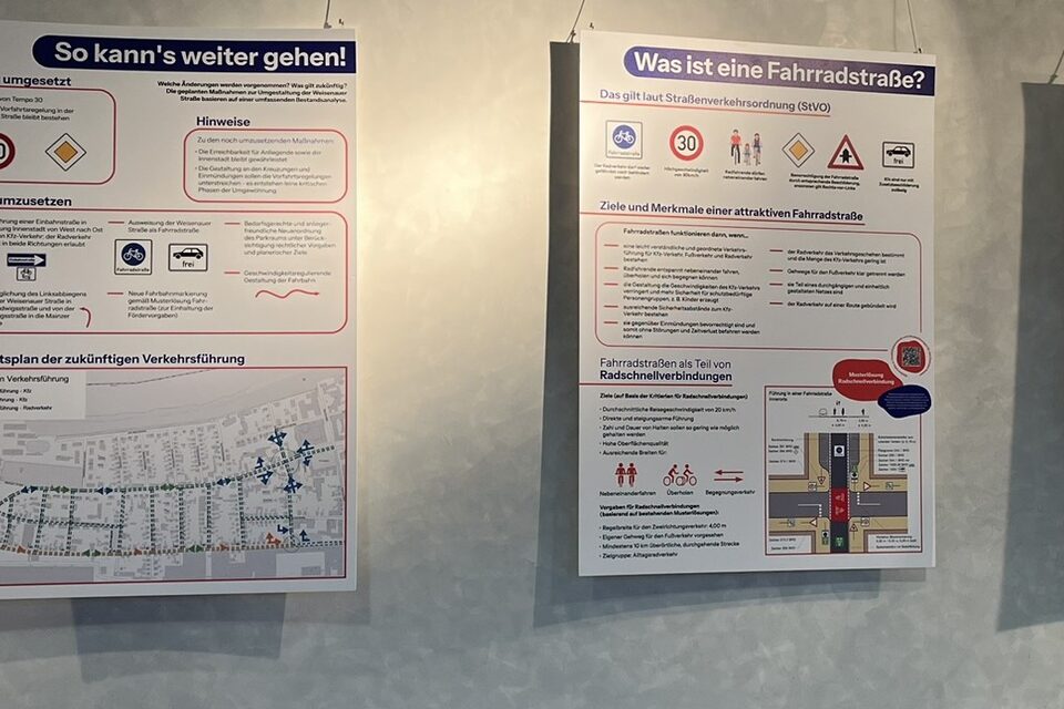 Informationstafeln "Was ist eine Fahrradstraße", die an einer grauen Wand hängen.