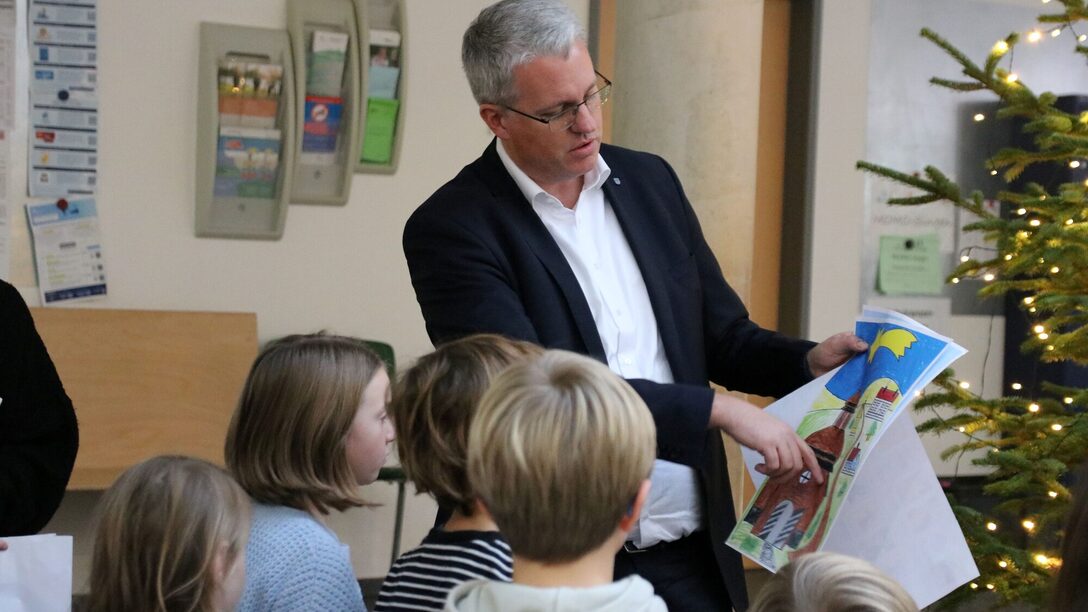 Oberbürgermeister Patrick Burghardt zeigt auf ein gemaltes Bild. Davor stehen Kinder, die man von hinten sieht.