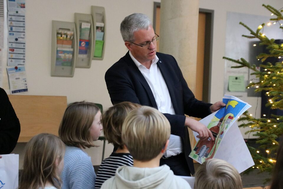 Oberbürgermeister Patrick Burghardt zeigt auf ein gemaltes Bild. Davor stehen Kinder, die man von hinten sieht.