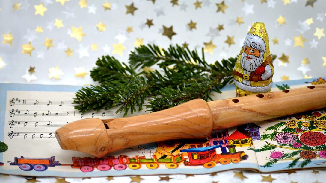 Liederheft mit Noten liegt auf Tischdecke mit Sternen. Darüber ein Tannenzweig, eine Blockflöte und ein Schokoladen-Nikolaus.
