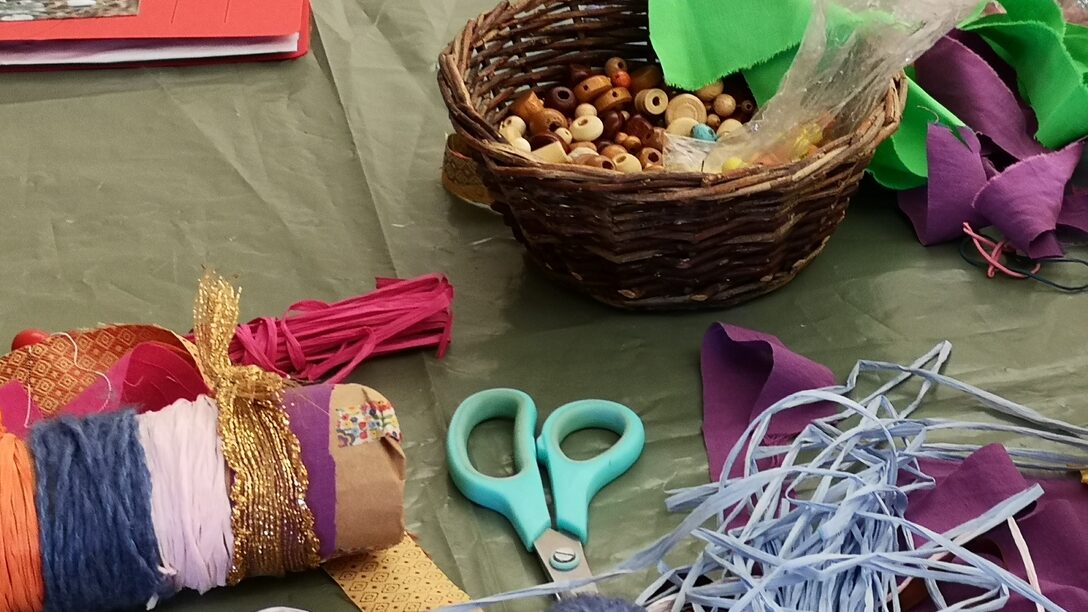 Bastelmaterialien wie Schere, Bänder und Perlen liegen auf einem Tisch bereit.