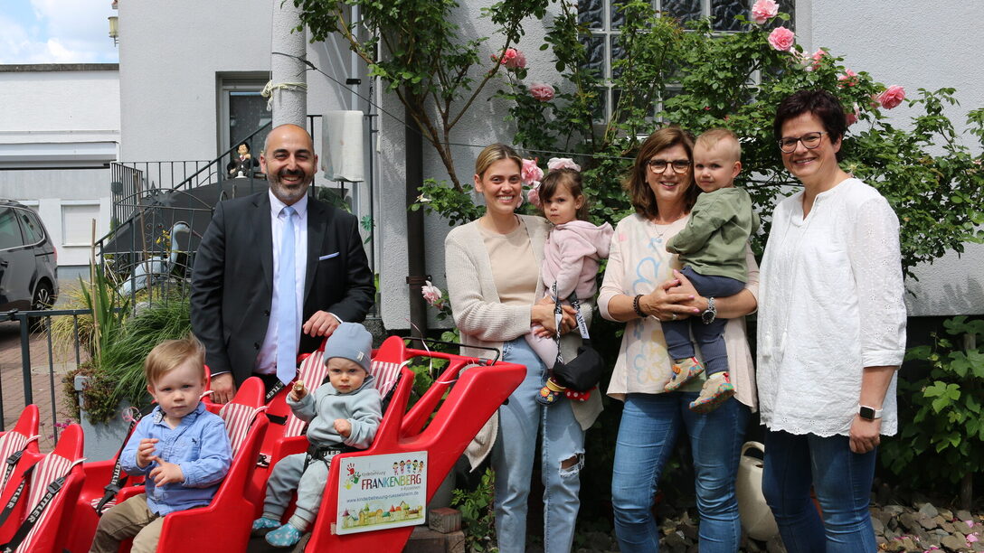 Mehrere Personen stehen vor und neben einem Bollerwagen mit Sitzen. Zu sehen sind vier Kinder und vier Erwachsene.