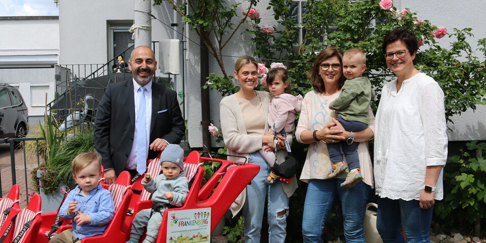 Mehrere Personen stehen vor und neben einem Bollerwagen mit Sitzen. Zu sehen sind vier Kinder und vier Erwachsene.