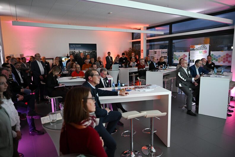 Mehrere Gewerbevertreter sitzen an weißen Tischen mit Barhockern und blicken aufmerksam nach vorne.