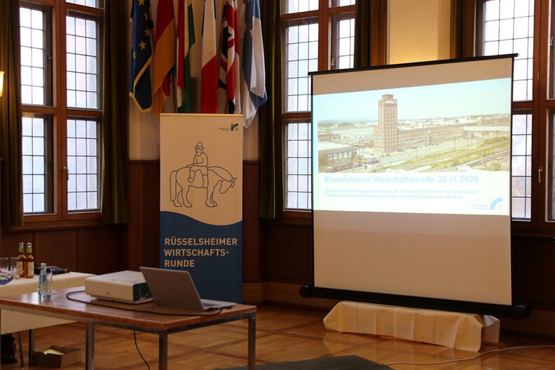 Blick in den Trausaal, in dem ein Rollup mit "Rüsselsheimer Wirtschaftsrunde" sowie eine Leinwand mit Präsentation aufgestellt sind.