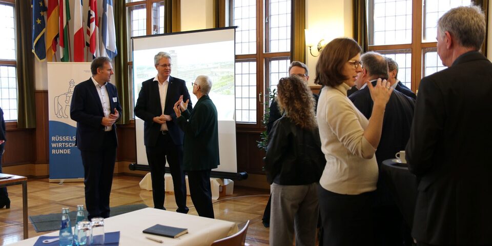 Blick in den Trausaal, in dem Teilnehmende der Wirtschaftsrunde in lockeren Grüppchen zusammenstehen und plaudern. Vor der Leinwand sind Maik Landwehr, Prof. Dr. Birgit Scheppath und OB Burghardt in ein Gespräch vertieft.
