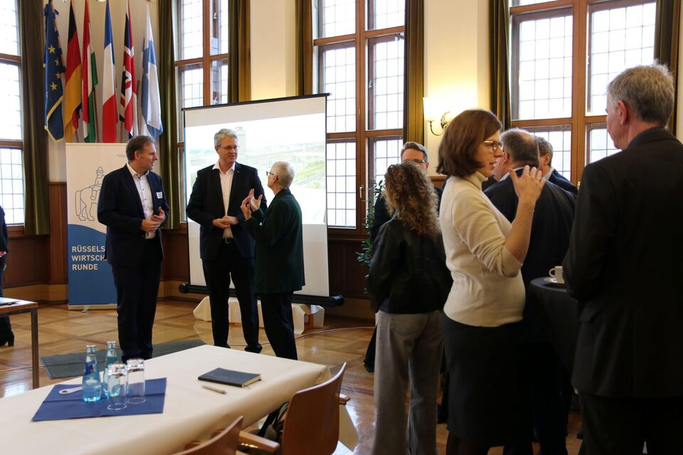 Blick in den Trausaal, in dem Teilnehmende der Wirtschaftsrunde in lockeren Grüppchen zusammenstehen und plaudern. Vor der Leinwand sind Maik Landwehr, Prof. Dr. Birgit Scheppath und OB Burghardt in ein Gespräch vertieft.