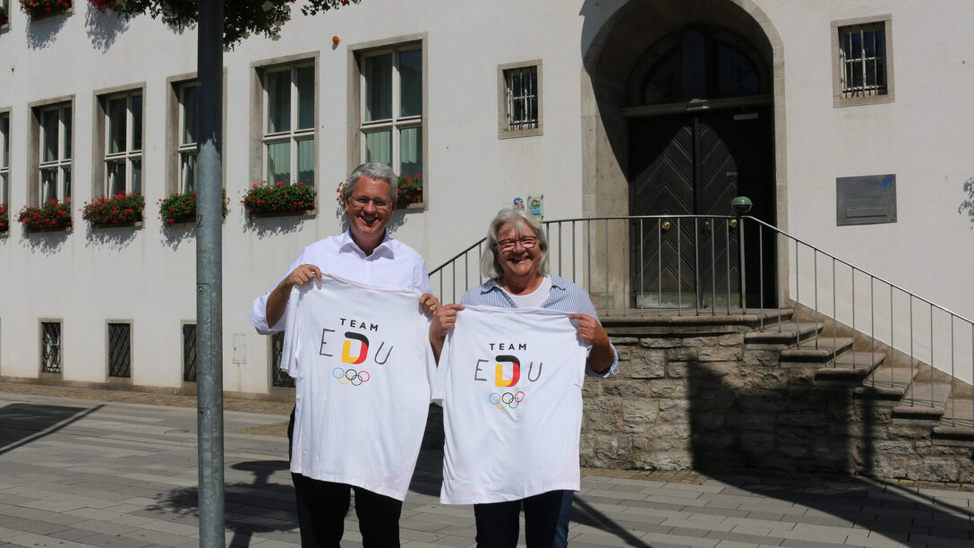 Oberbürgermeister Patrick Burghardt und Anette Tettenborn (Fachbereichsleitung Sport und Ehrenamt) halten "Team EDU"-T-Shirts.