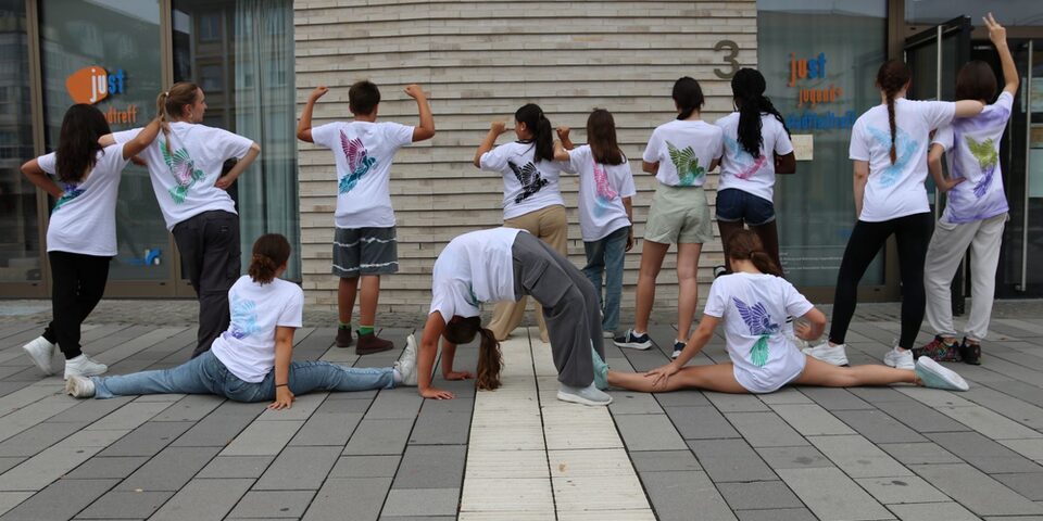 Teilnehmende der Summer Dance Days von hinten mit selbstgestalteten T-Shirts und in verschiedenen Tanzposen. Vor dem Jugend- und Stadtteiltreff.