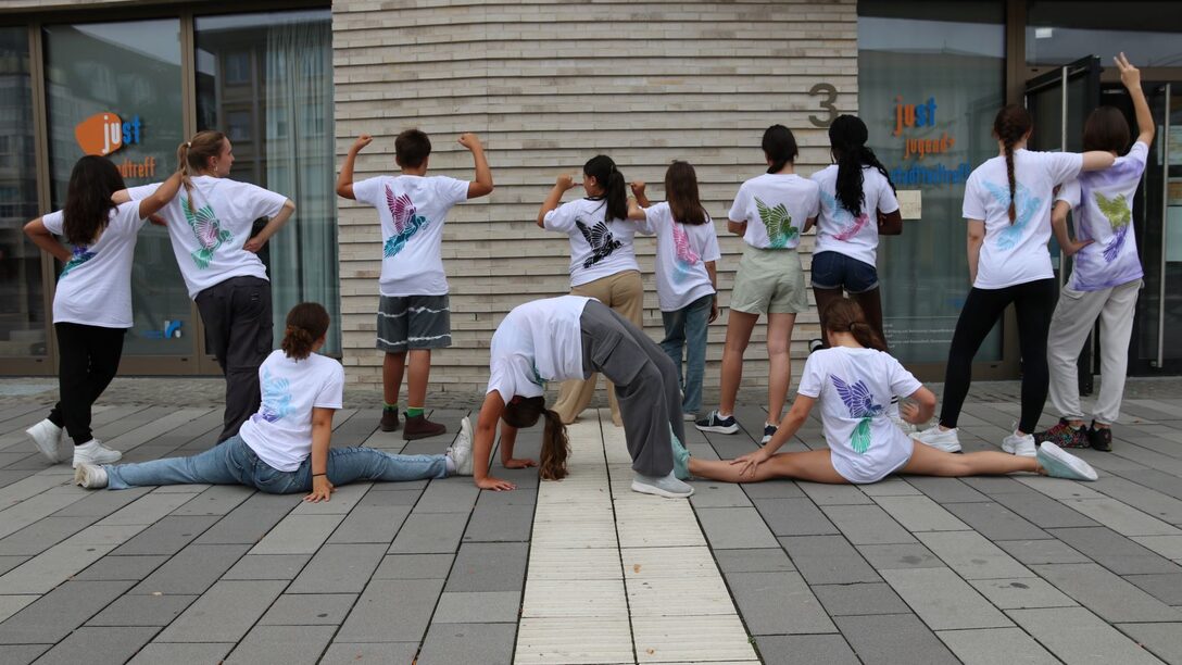 Teilnehmende der Summer Dance Days von hinten mit selbstgestalteten T-Shirts und in verschiedenen Tanzposen. Vor dem Jugend- und Stadtteiltreff.