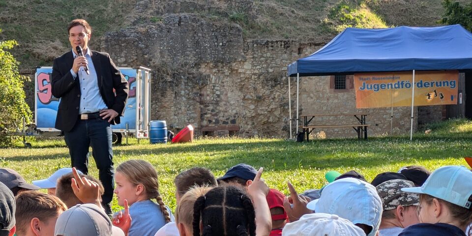 Bürgermeister Dennis Grieser eröffnet die Ferienspiele. Im Vordergrund sind einige Kinder zu sehen.