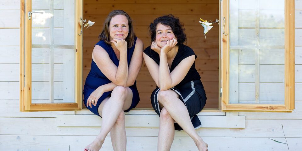 Zwei Frauen sitzen auf dem Fensterbrett eines geöffneten Fensters