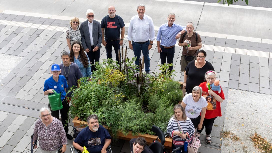Oberbürgermeister Patrick Burghardt, Mitglieder des LIONS Club, Steffen Walther und Bewohnerinnen und Bewohner des Herta-Max-Hauses der WfB Rhein-Main e.V stehen um das Rolli-Beet an der Friedensstraße.