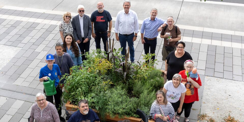 Oberbürgermeister Patrick Burghardt, Mitglieder des LIONS Club, Steffen Walther und Bewohnerinnen und Bewohner des Herta-Max-Hauses der WfB Rhein-Main e.V stehen um das Rolli-Beet an der Friedensstraße.