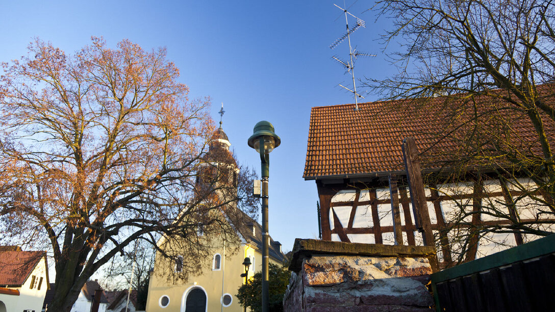 Blick auf den Platz "An der Wied": Im Zentrum die Kirche, daneben eine historische Straßenlaterne und ein Fachwerkhaus.
